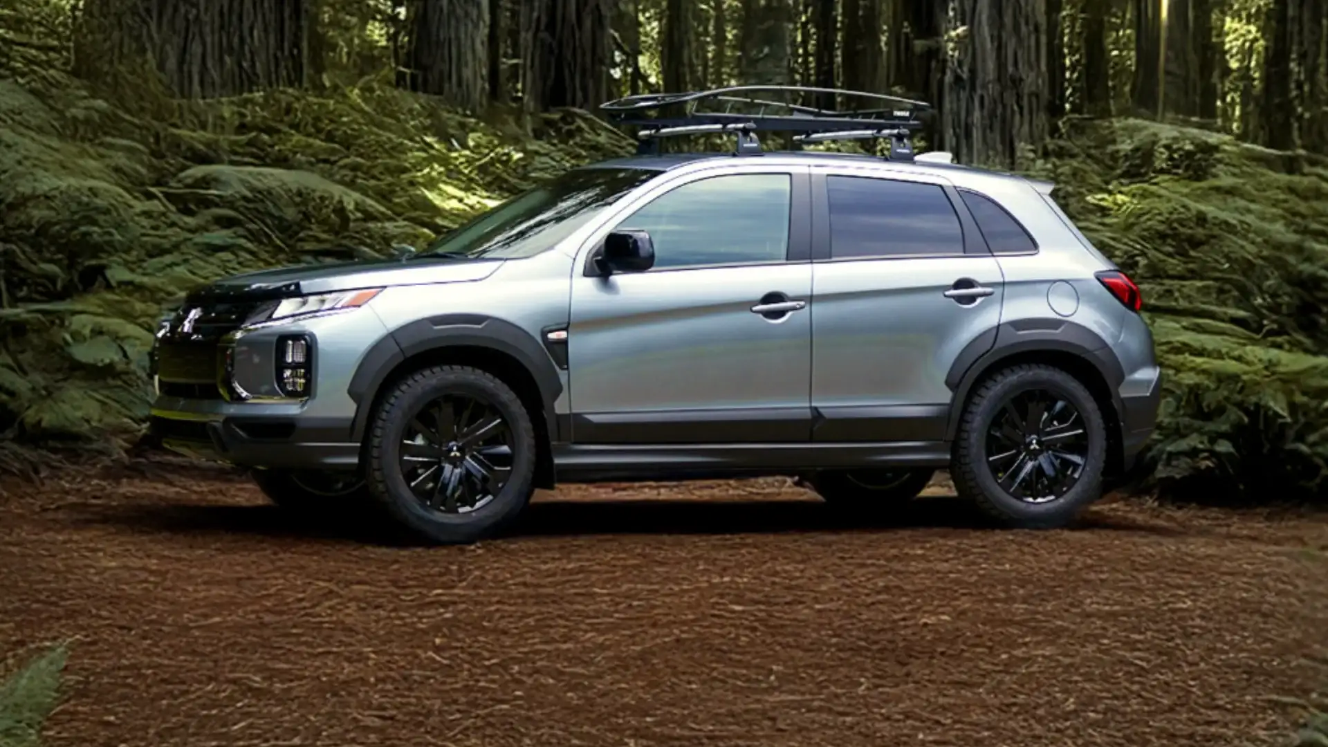2026 Mitsubishi Outlander Sport silver SUV side profile parked in forest with black wheels and rack