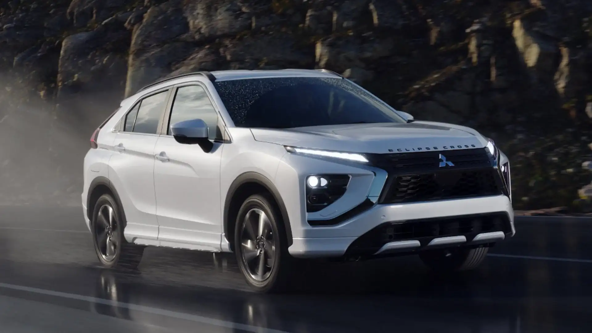 2026 Mitsubishi Eclipse Cross in white driving on a wet road with bright LED headlights illuminated.