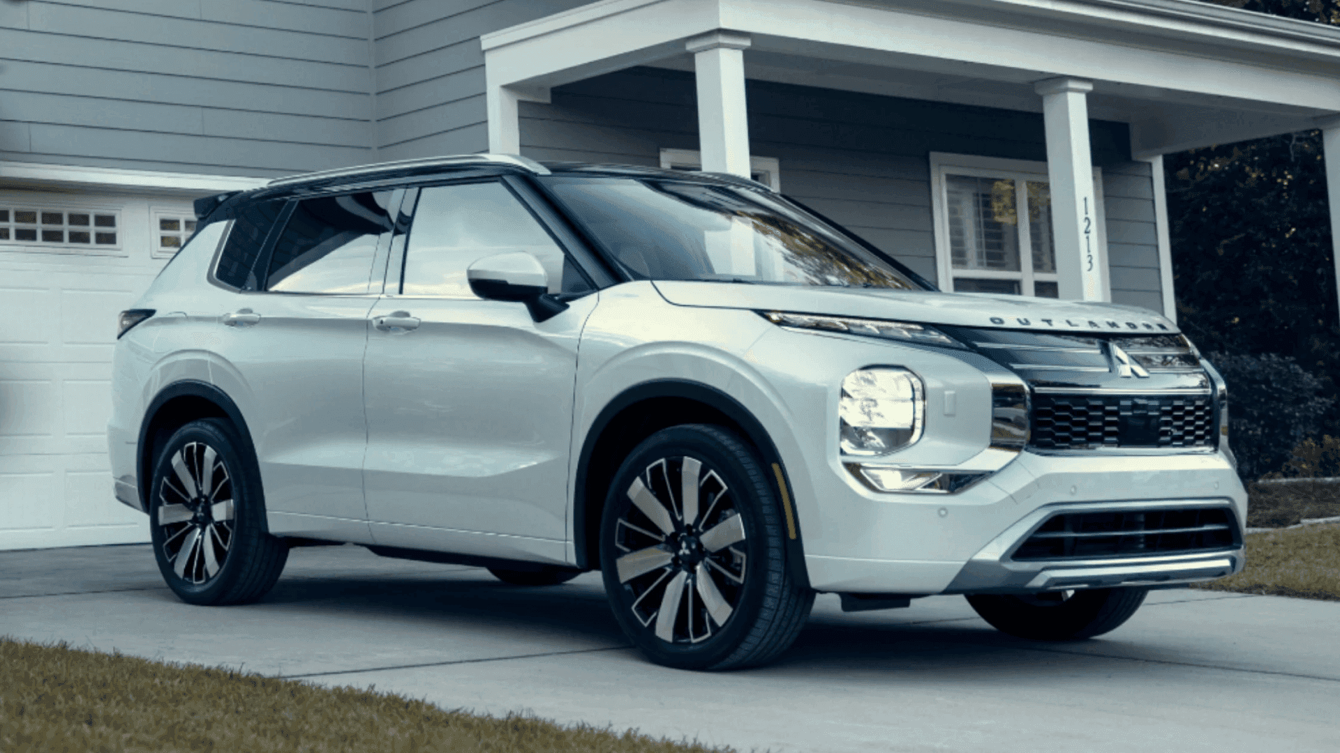 2026 Mitsubishi Outlander in white parked in the driveway outside a suburban home with a black roof.