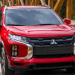 2026 Mitsubishi Outlander Sport in red driving across wooden bridge with bold grille and headlights.