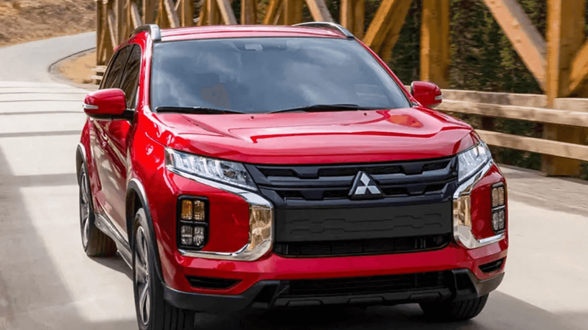 2026 Mitsubishi Outlander Sport in red driving across wooden bridge with bold grille and headlights.