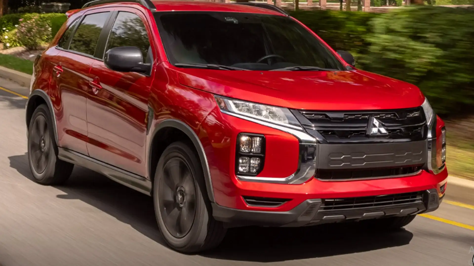 2026 Mitsubishi Outlander Sport red SUV cruising on a road with black wheels and bold front styling.