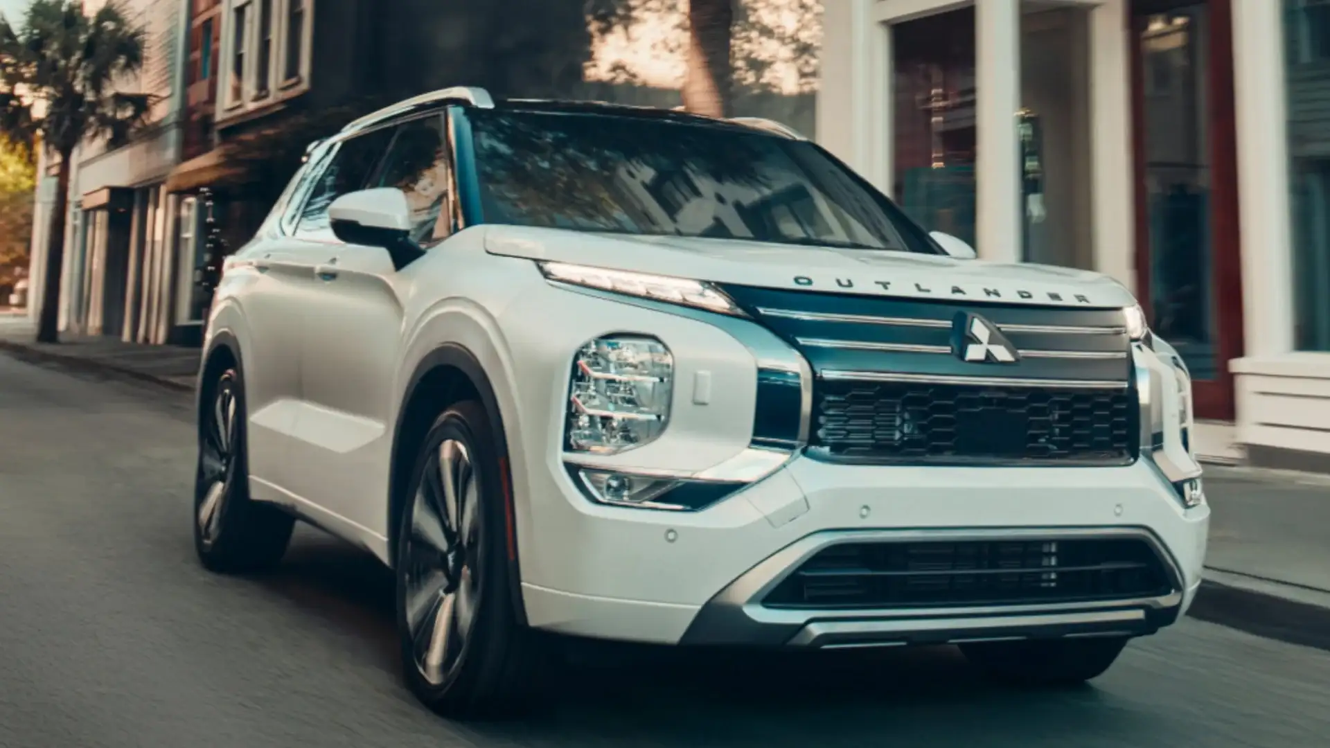 2026 Mitsubishi Outlander in white driving through city streets with a bold grille and LED lighting.