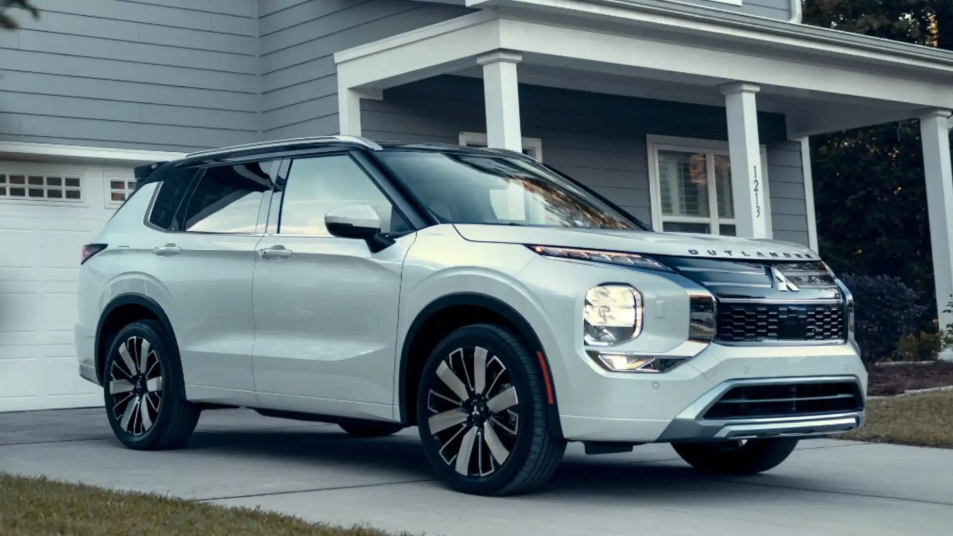 2026 Mitsubishi Outlander white SUV parked in a driveway before a modern suburban home in three-quarter view.