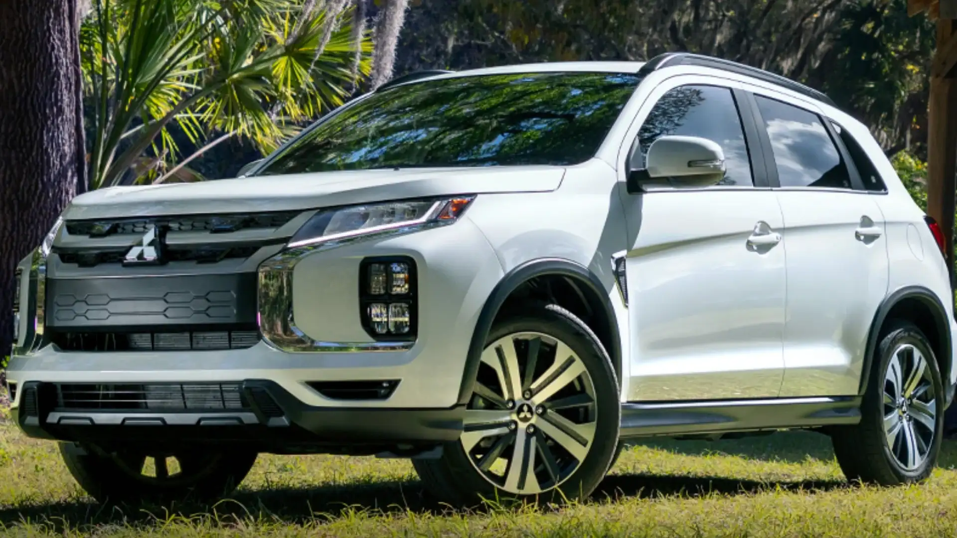 2026 Mitsubishi Outlander white SUV driving through a downtown city street in a front three-quarter view.