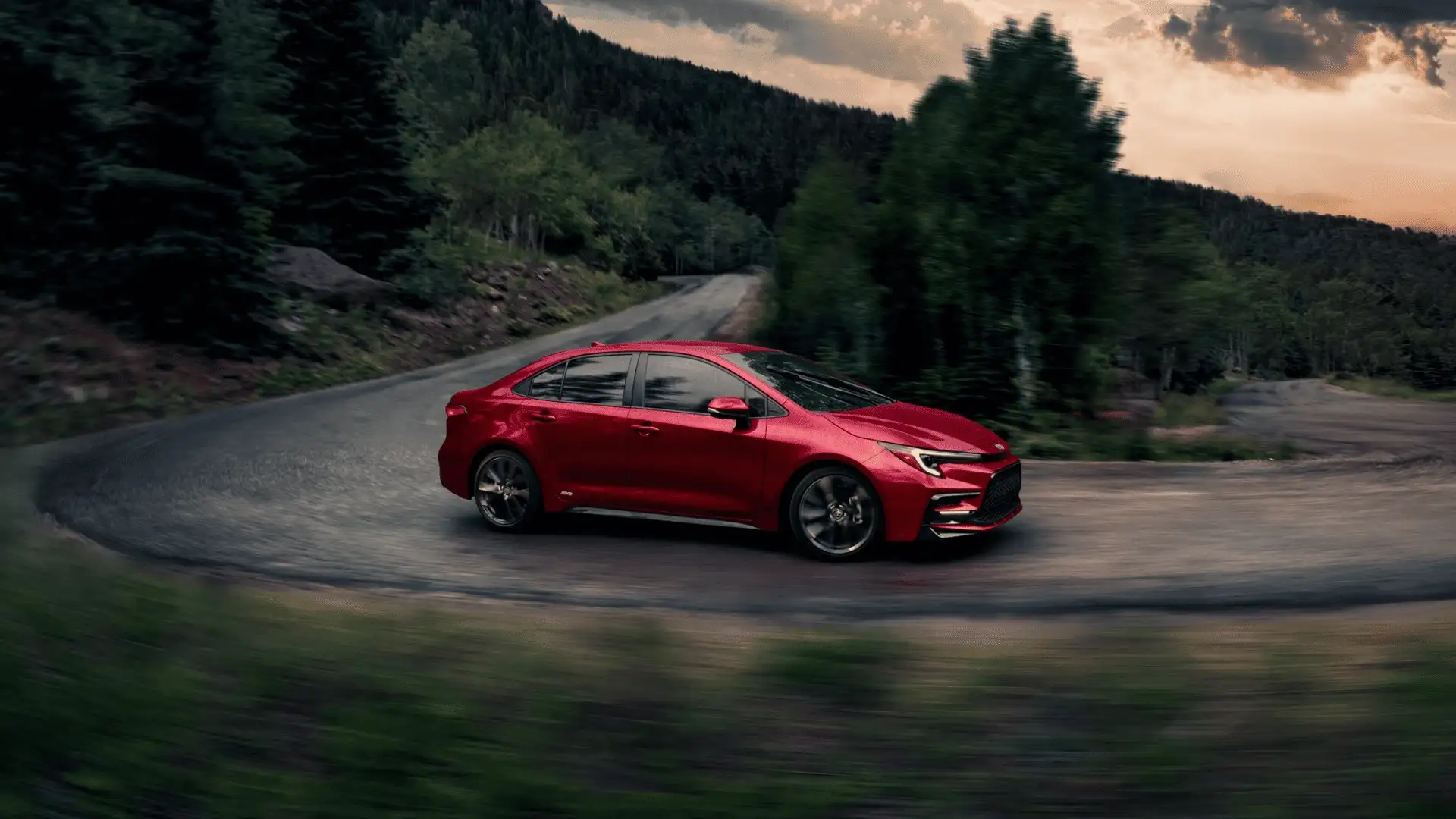 Red 2025 Toyota Corolla Hybrid driving on a scenic road near Hagerstown, MD, highlighting fuel efficiency and sleek exterior design.