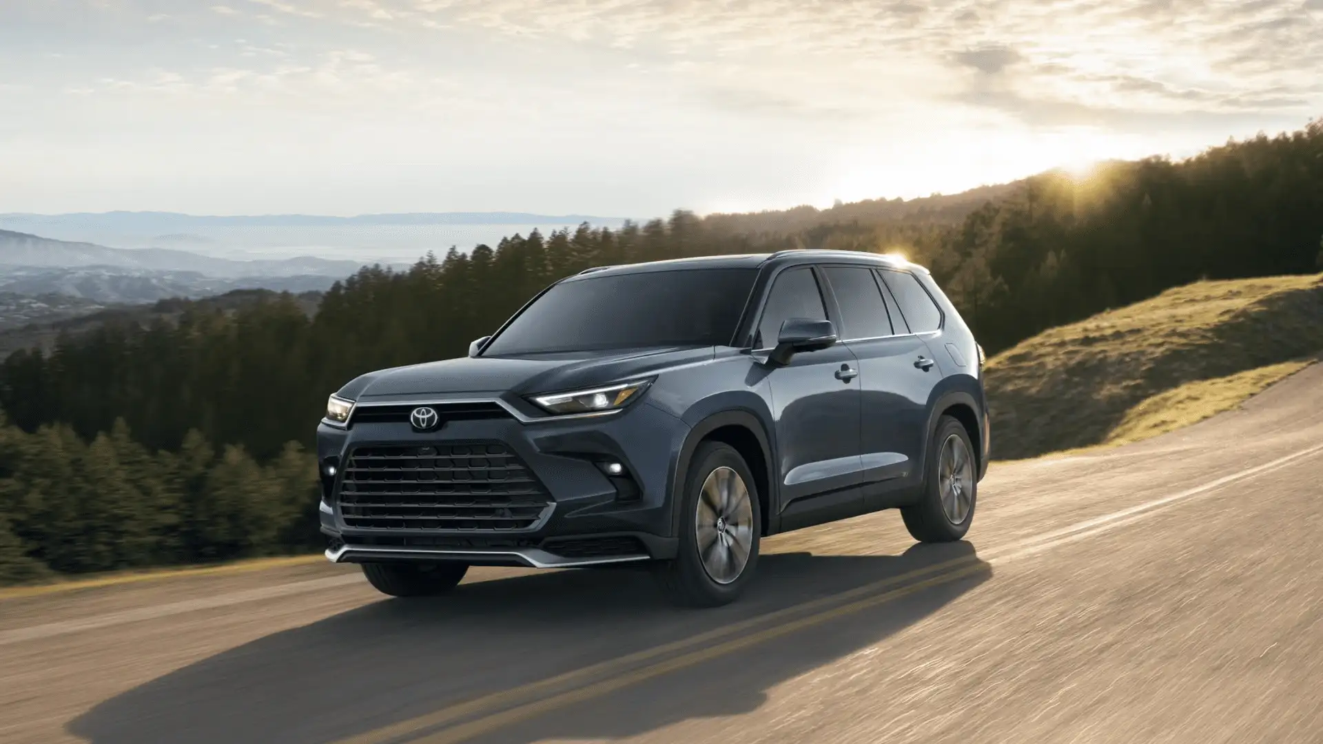 Gray 2025 Toyota Grand Highlander driving through a scenic landscape near Hagerstown, MD, showcasing its spacious SUV design.
