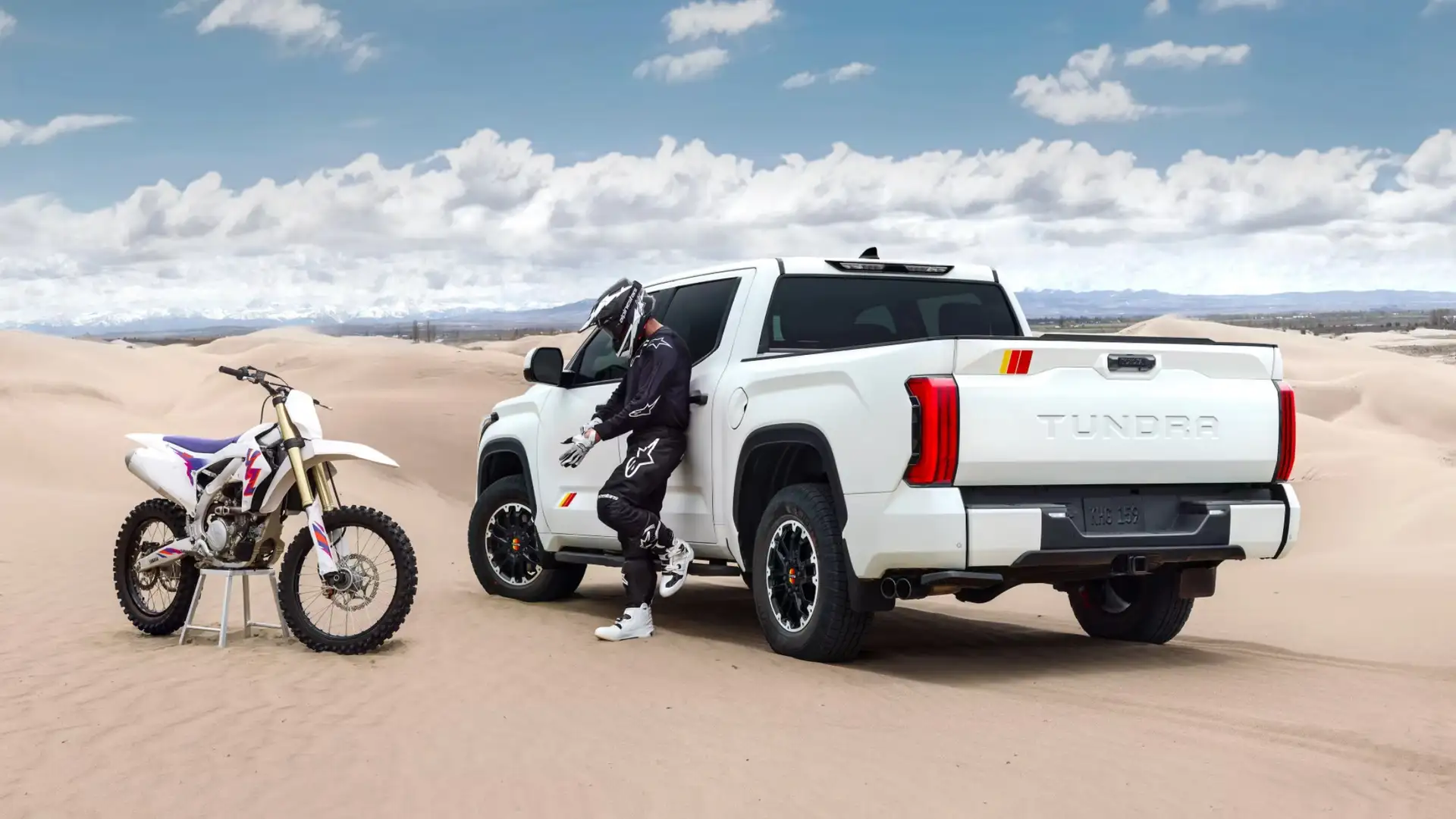 2025 Toyota Tundra power and performance shown with a white pickup truck parked in the desert next to a dirt bike, highlighting towing strength and off road capability.