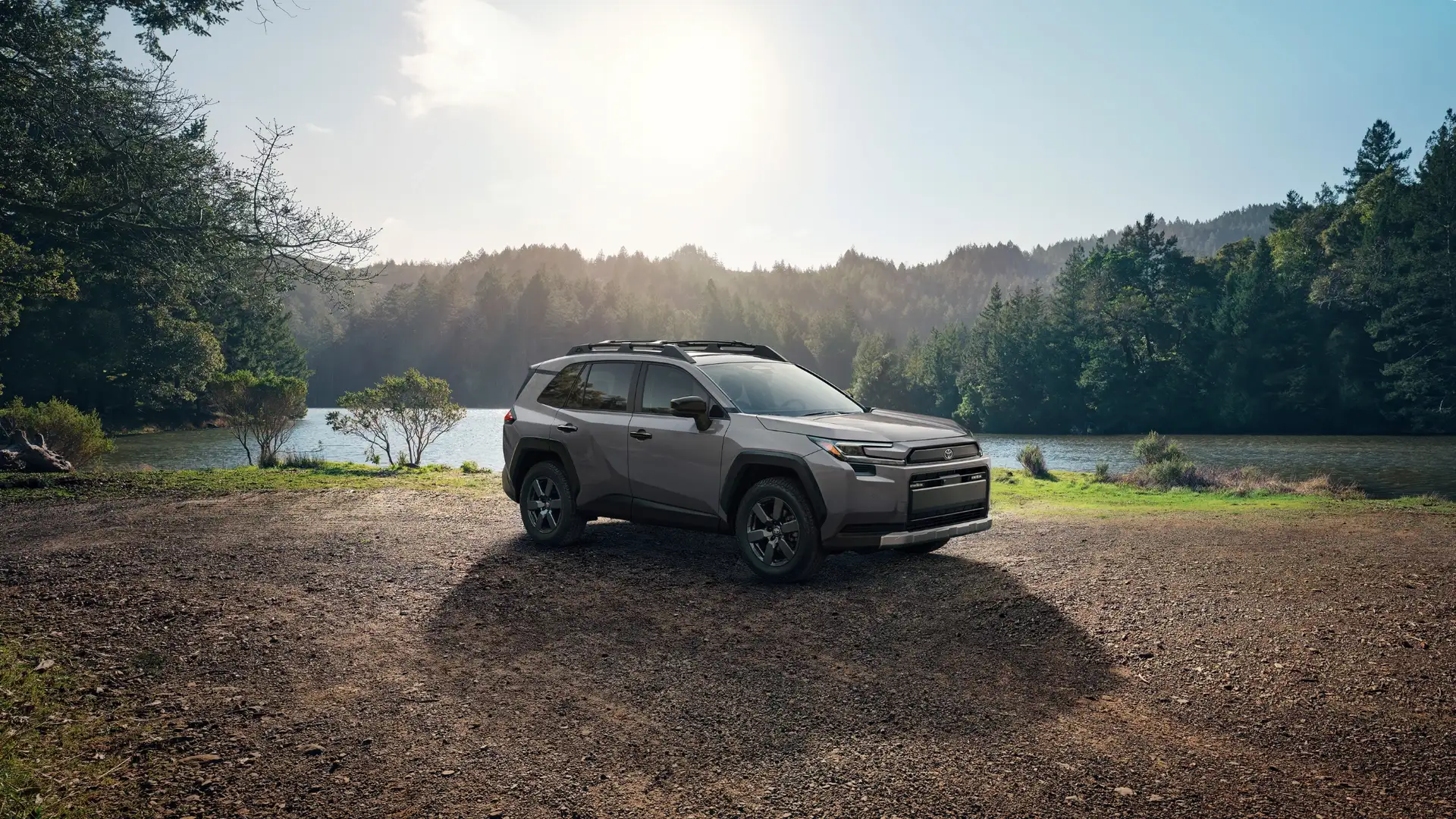 2026 Toyota RAV4 parked near a lake and wooded area, highlighting rugged exterior design and adventure-ready capability.