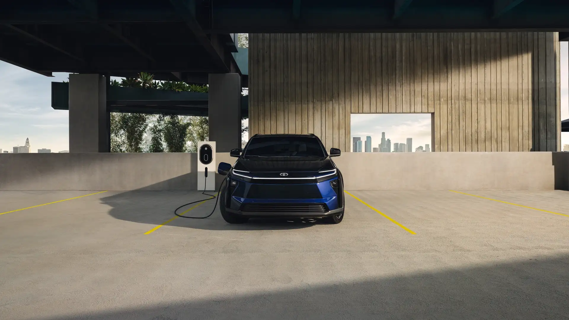 2026 Toyota bZ electric vehicle charging in a modern parking structure, showcasing EV design, front lighting, and charging port connection.