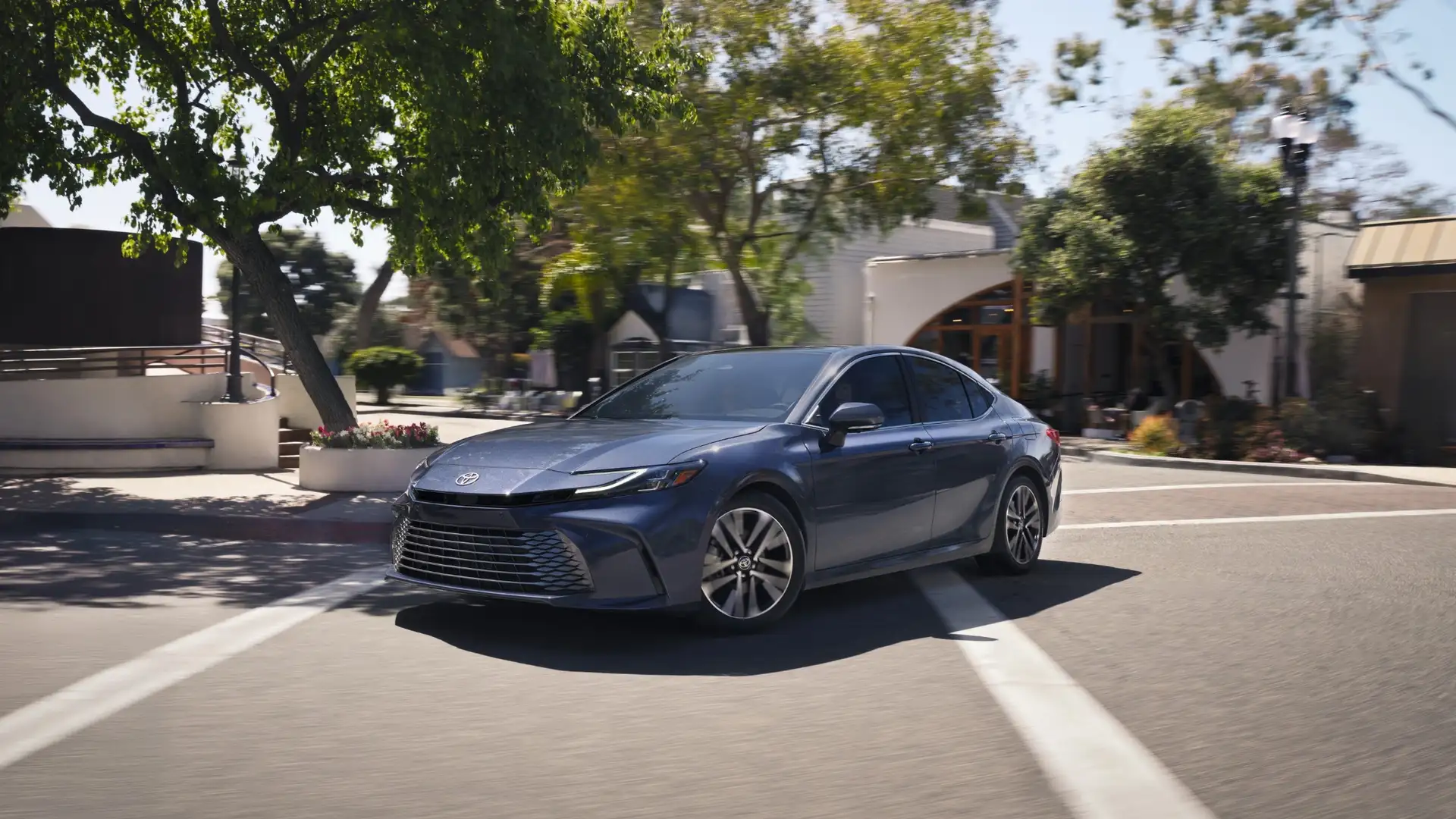 2025 Toyota Corolla Cross driving on a tree-lined road, showcasing family-friendly space and versatility for drivers in Greencastle PA.