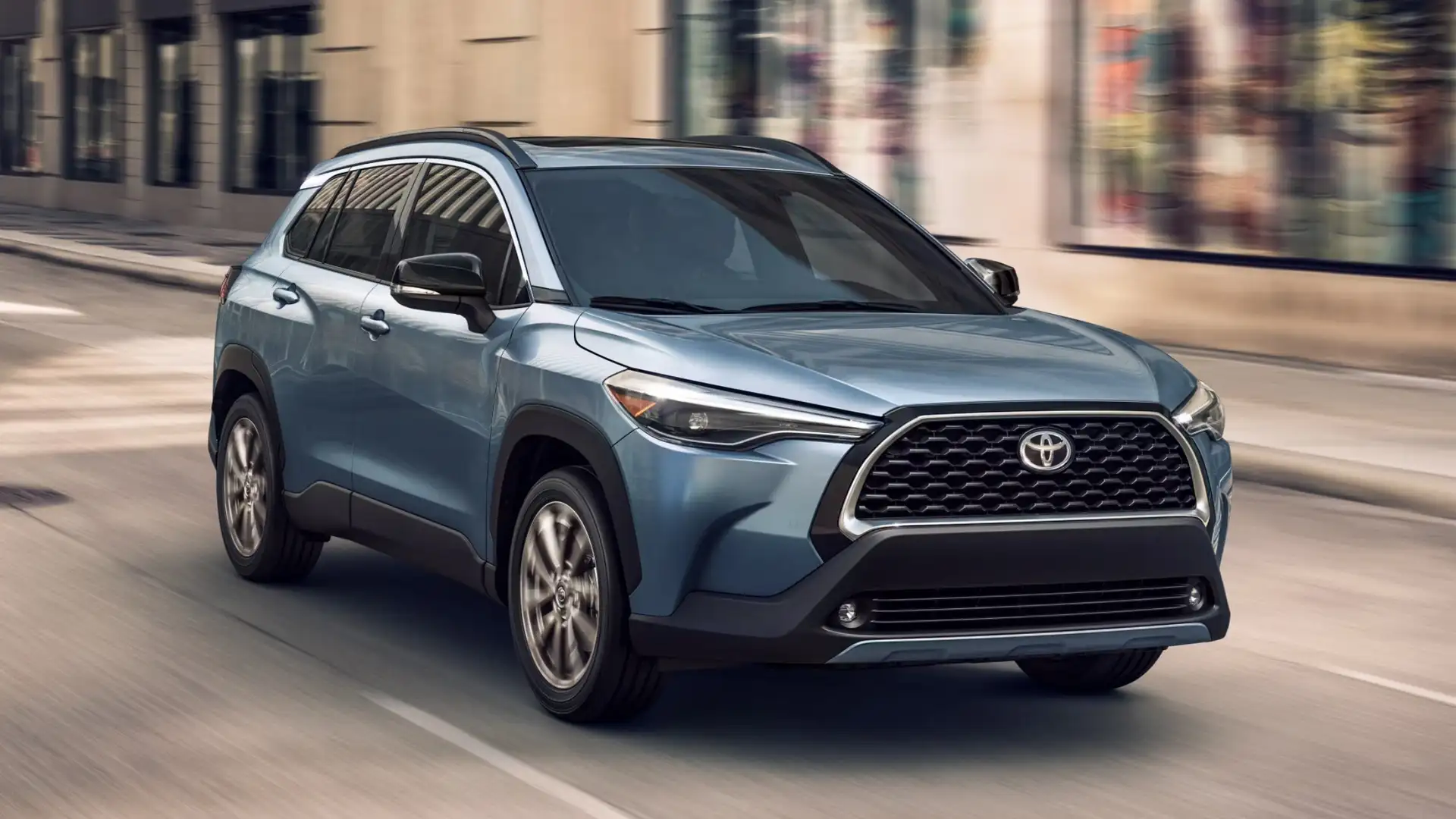 2025 Toyota Corolla Cross driving through a city street, showcasing modern design and multimedia technology for Hagerstown commuters.