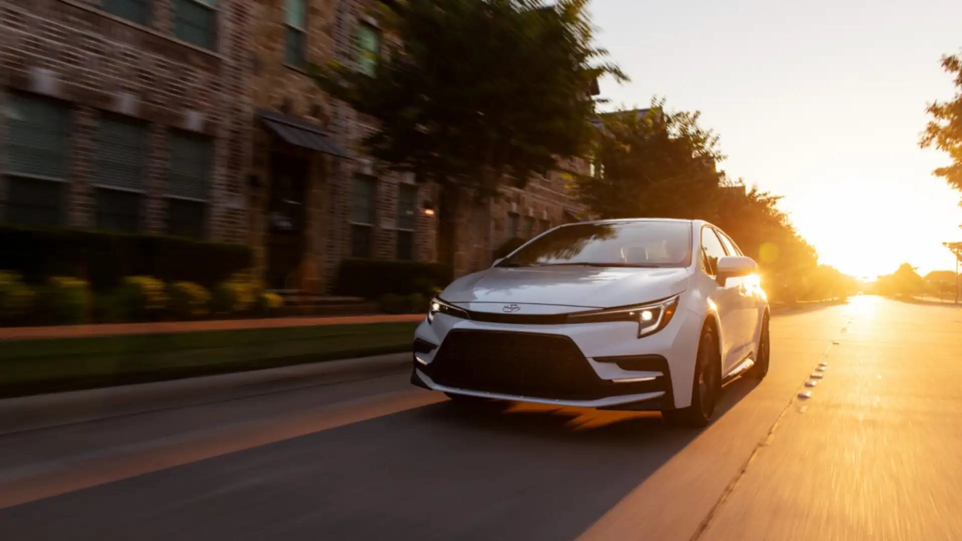 White 2025 Toyota Corolla driving through a residential street at sunset, highlighting smooth ride quality and modern exterior design for Hagerstown, MD drivers.