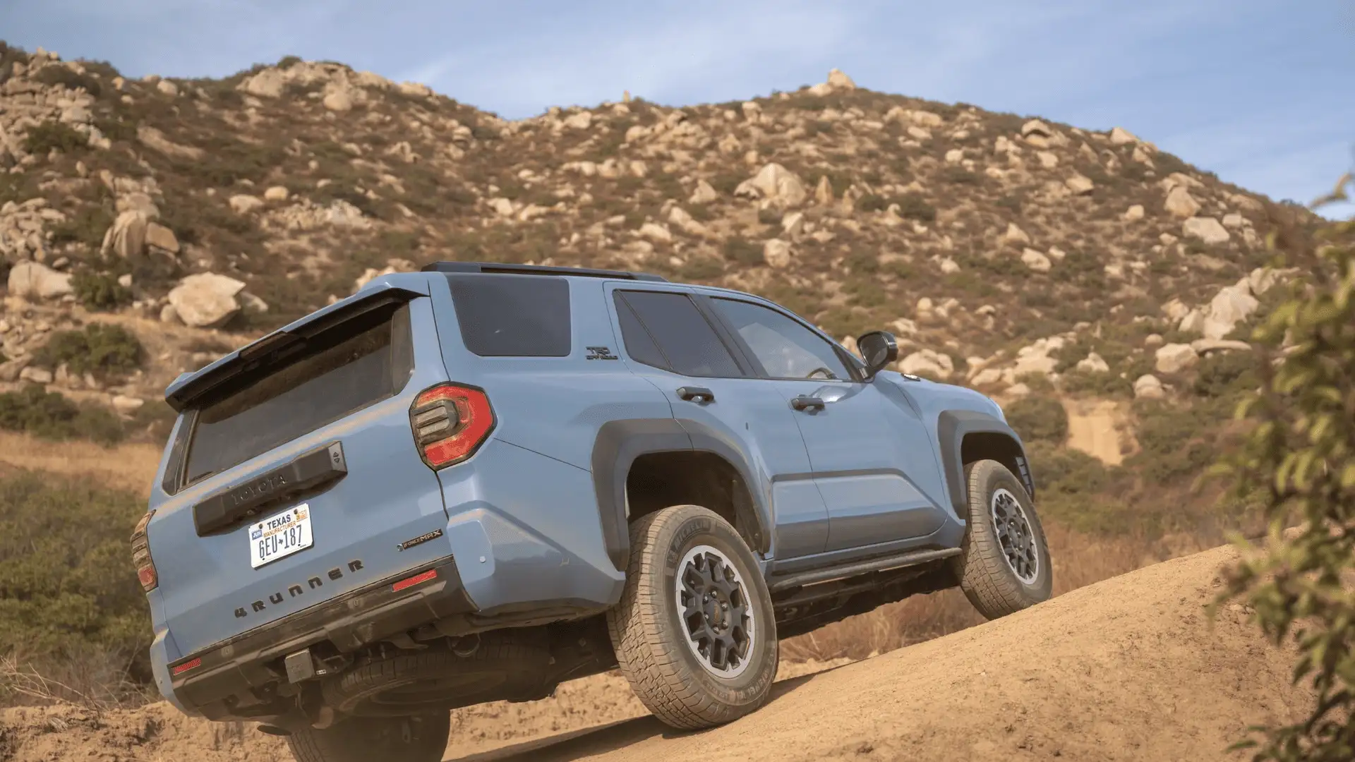 Blue 2026 Toyota 4Runner climbing a dirt hill, highlighting ground clearance, off-road angles, and rugged trail performance.