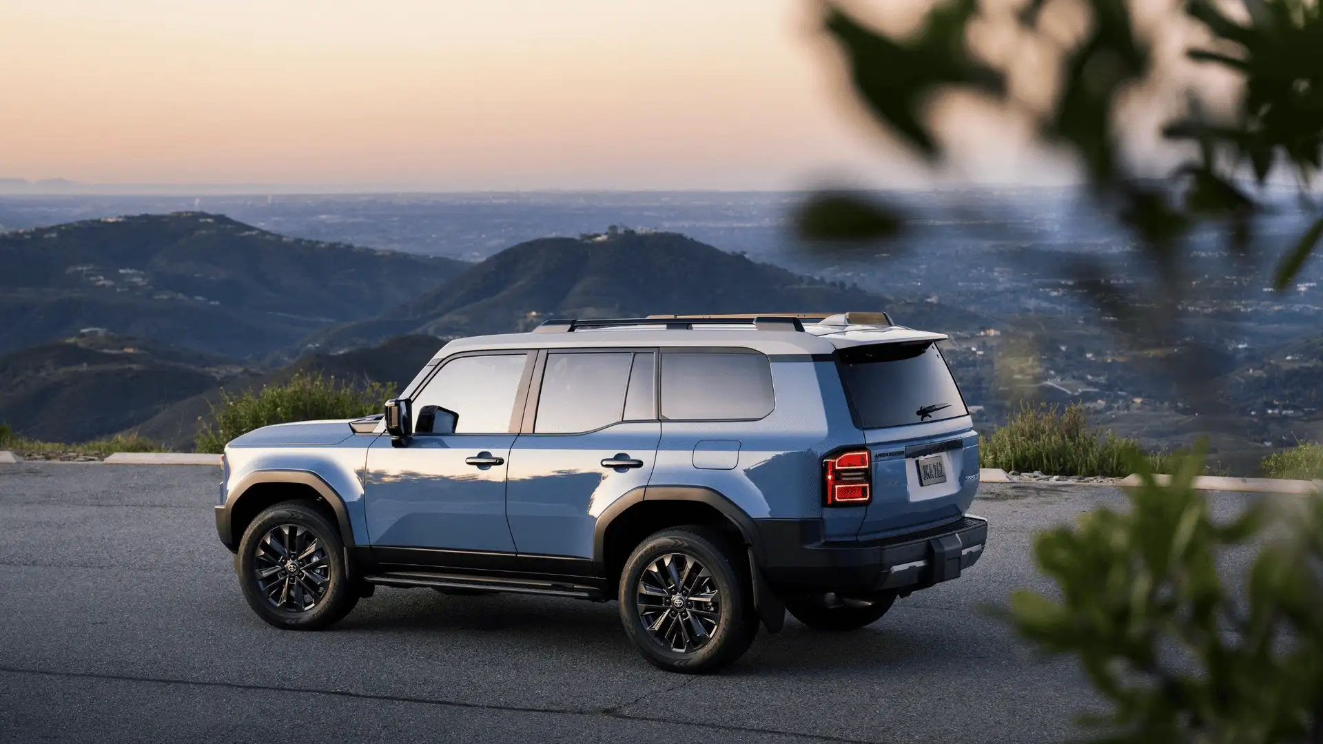 Side view of a blue 2026 Toyota Land Cruiser parked on a scenic overlook, highlighting its SUV body proportions and exterior structure.
