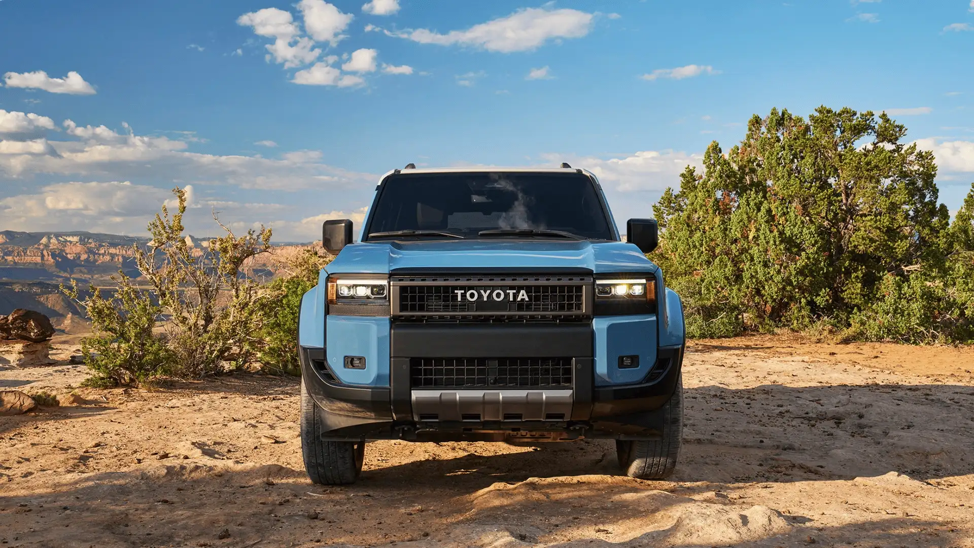 Front view of a blue 2026 Toyota Land Cruiser parked on rugged terrain near Hagerstown, MD, showcasing its bold grille and off-road SUV design.