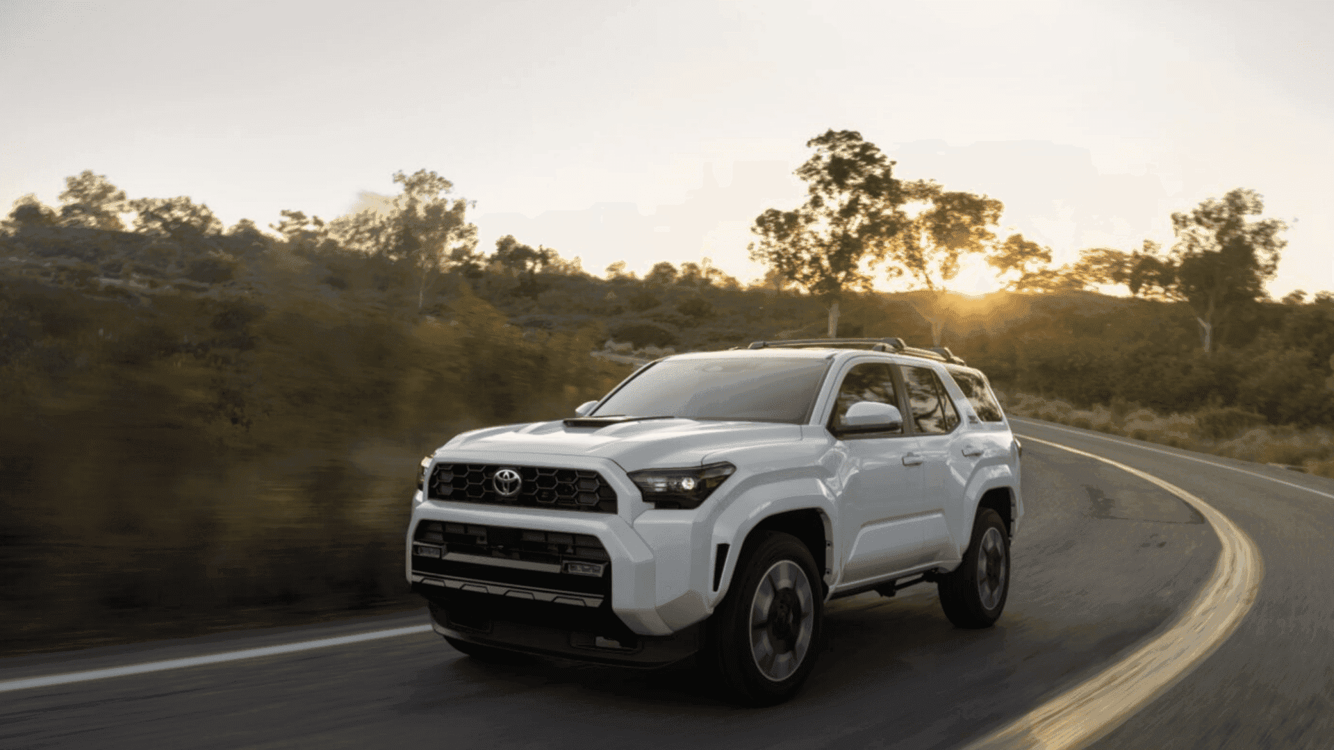 White 2026 Toyota 4Runner SUV driving on a winding road at sunset near Hagerstown, MD, highlighting rugged performance and off-road capability.