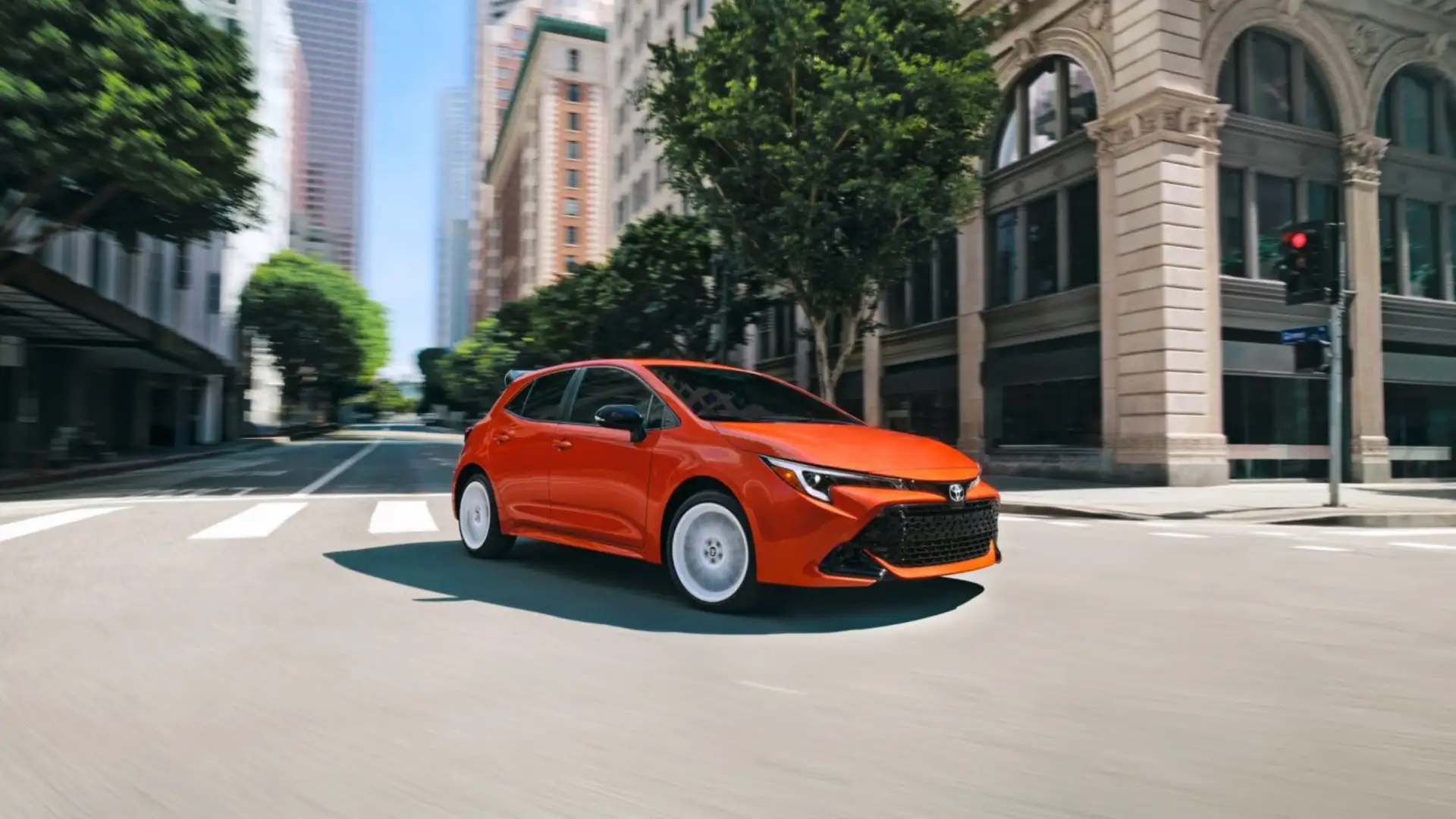2026 Toyota Corolla Hatchback in orange driving through a city intersection in Hagerstown, MD.