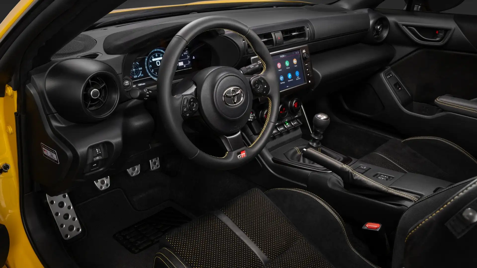 2026 Toyota GR86 sport interior with GR-branded steering wheel, manual shifter, aluminum pedals, and touchscreen infotainment system