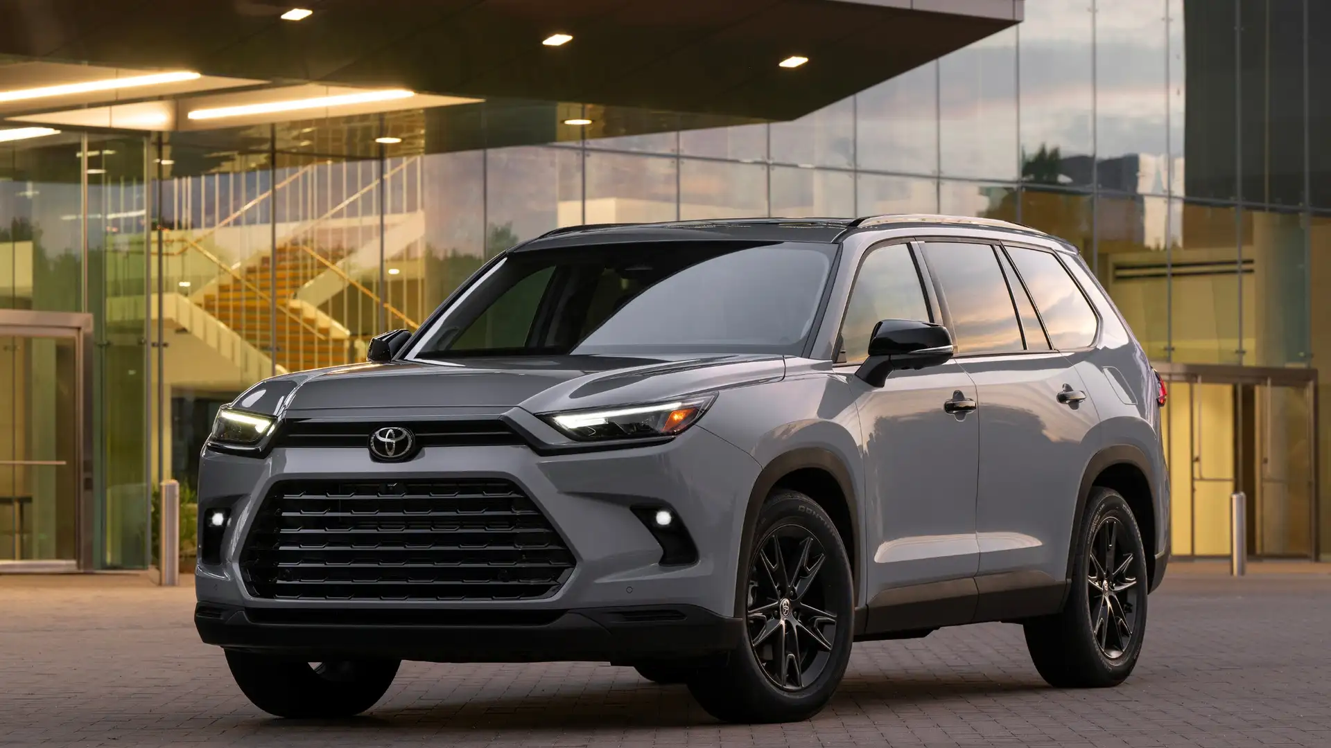 2026 Toyota Grand Highlander in grey with black wheels parked in front of a modern glass building, available in Hagerstown MD