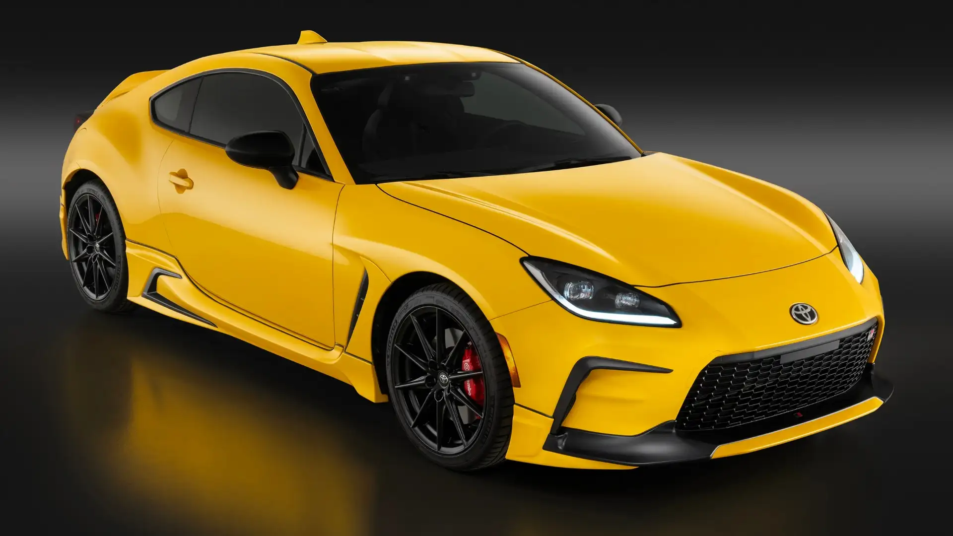 2026 Toyota GR86 in yellow with red Brembo brakes and black wheels on a dark studio background, showcasing responsive steering for Hagerstown MD backroads