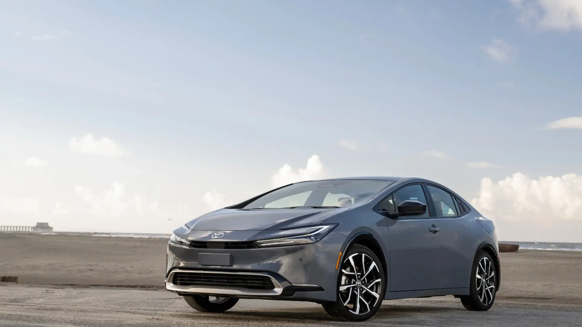 2026 Toyota Prius plug-in hybrid sedan in gray with silver alloy wheels parked on coastal beach with ocean and pier in background in Hagerstown MD
