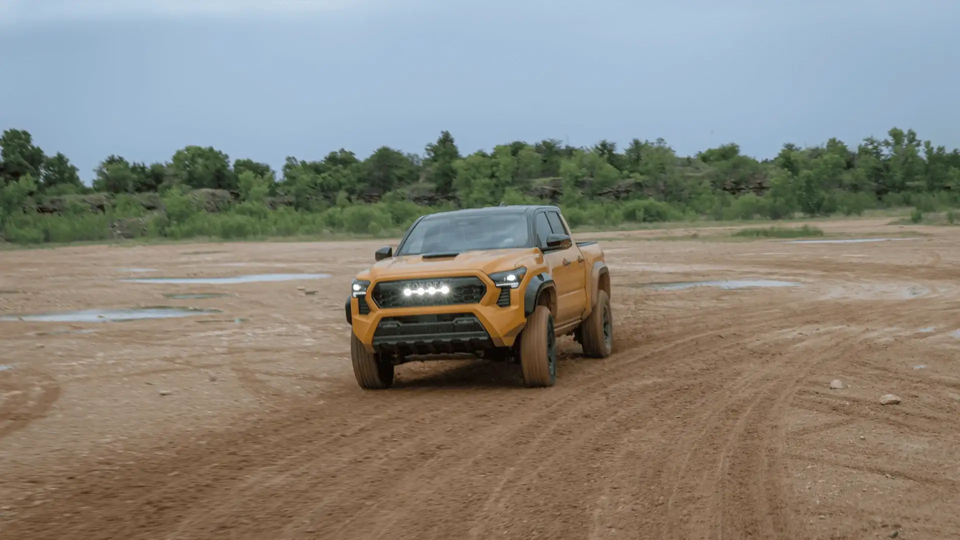 Orange 2027 Toyota pickup truck driving muddy dirt trail in Hagerstown MD