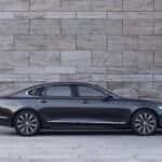 2025 Volvo S90 luxury sedan side profile in metallic gray parked against modern stone wall