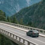 2025 Volvo XC60 SUV rear three quarter view driving across bridge with sleek Scandinavian design